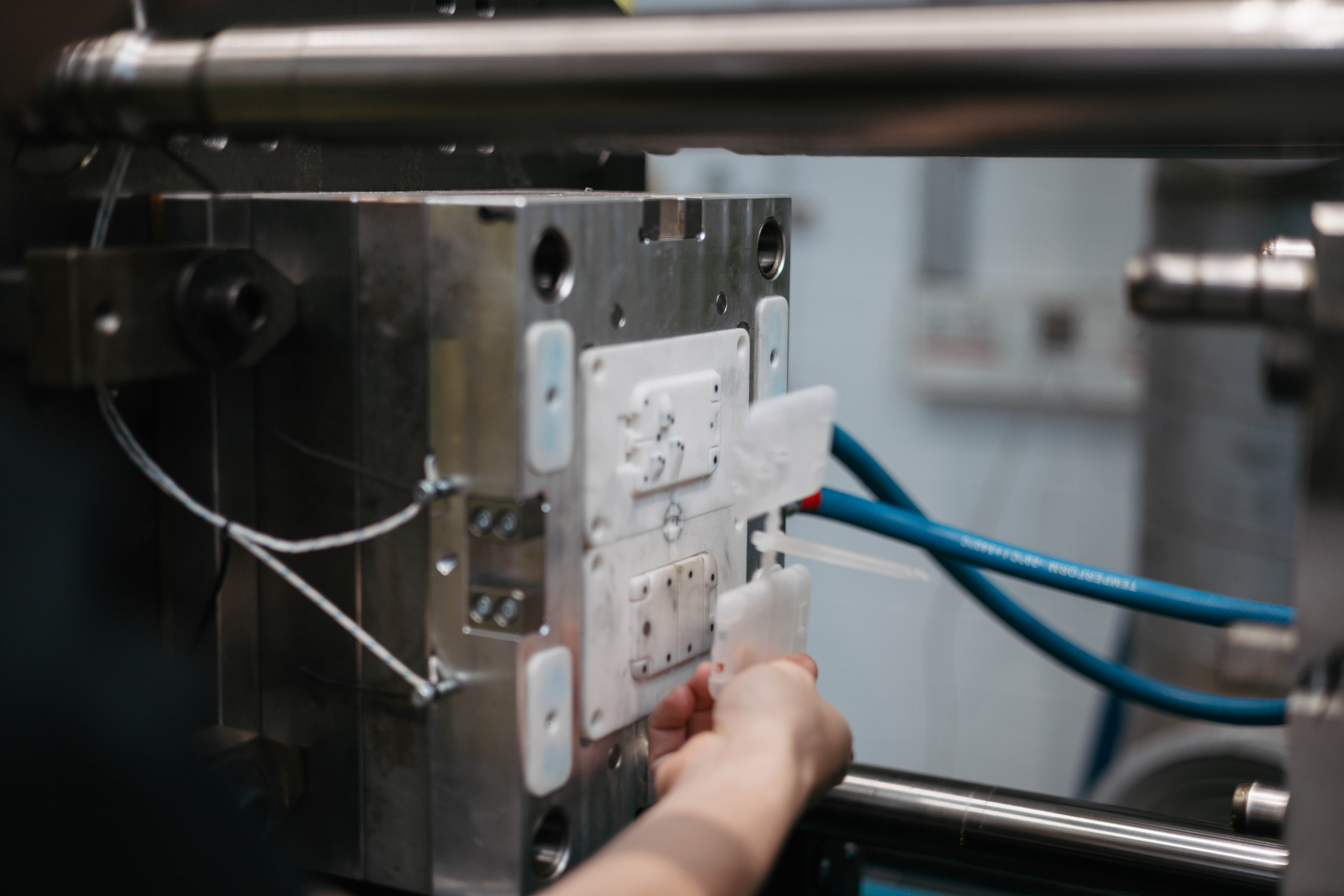 Eine Hand entnimmt 2 weiße Plättchen, die noch über den Anguss verbunden sind, aus einer Spritzgießform