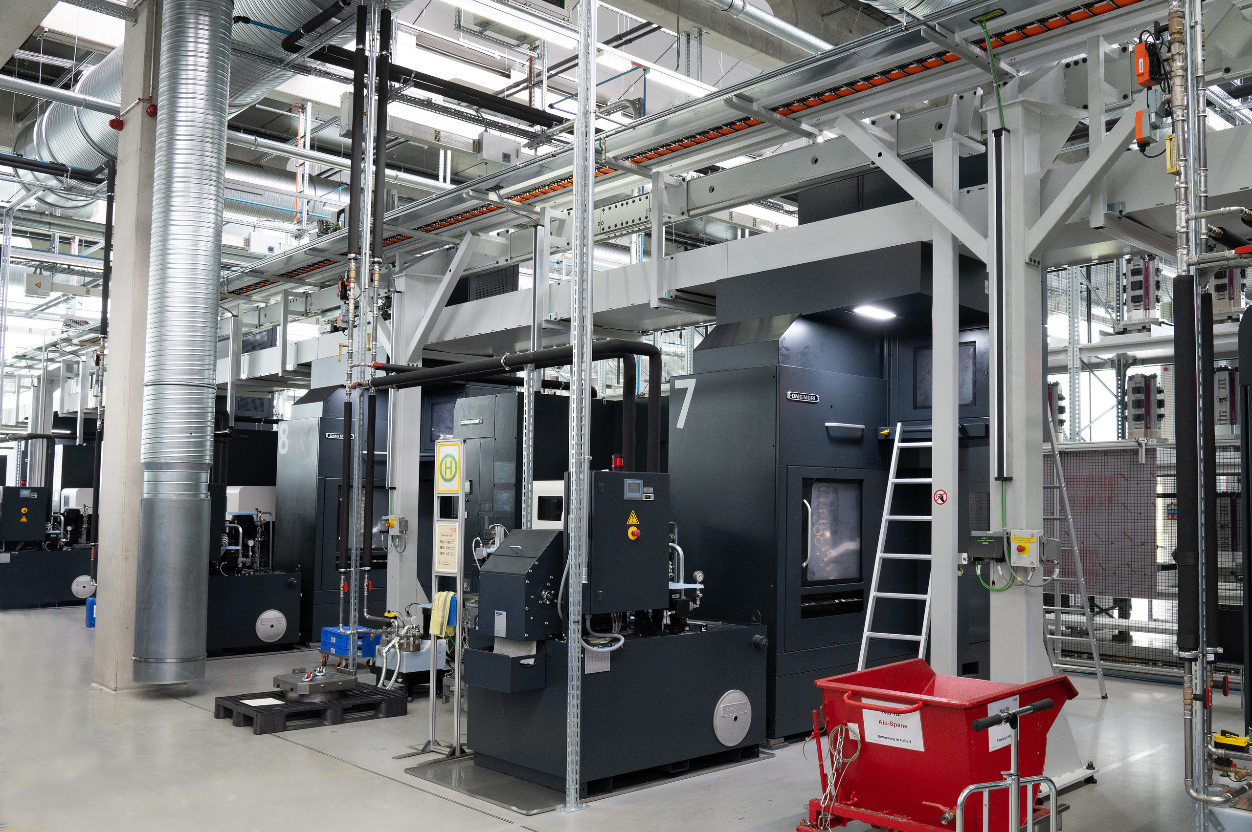 <p>Zu sehen ist eine Produktionshalle mit mehreren großen CNC-Bearbeitungsmaschinen samt Absaug- und Versorgungsinfrastruktur sowie einem Spänebehälter.<p>