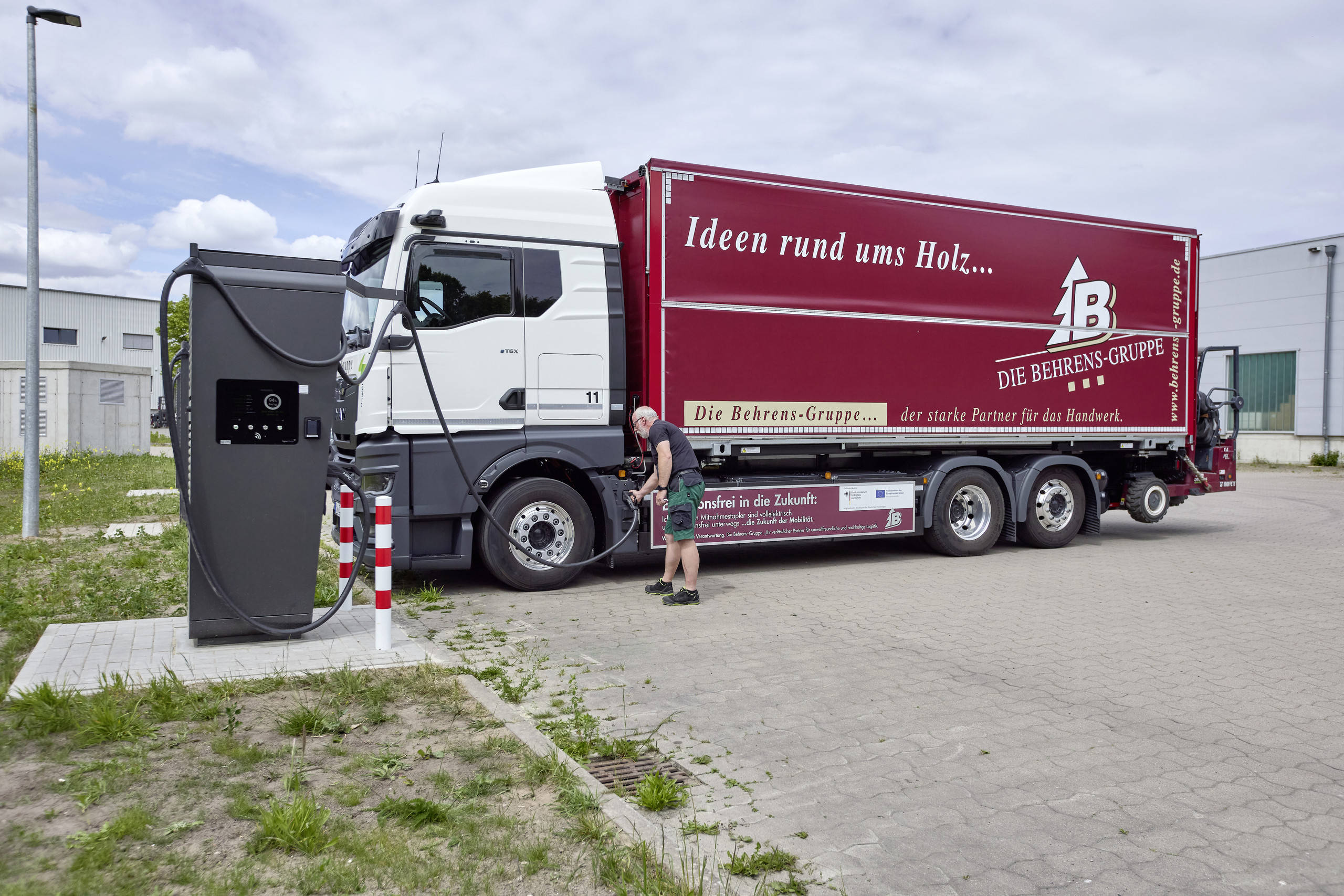 ein E-Lkw der Spedition Behrens an einer Ladesäule,  Fahrer mit Hand am Ladeanschluss