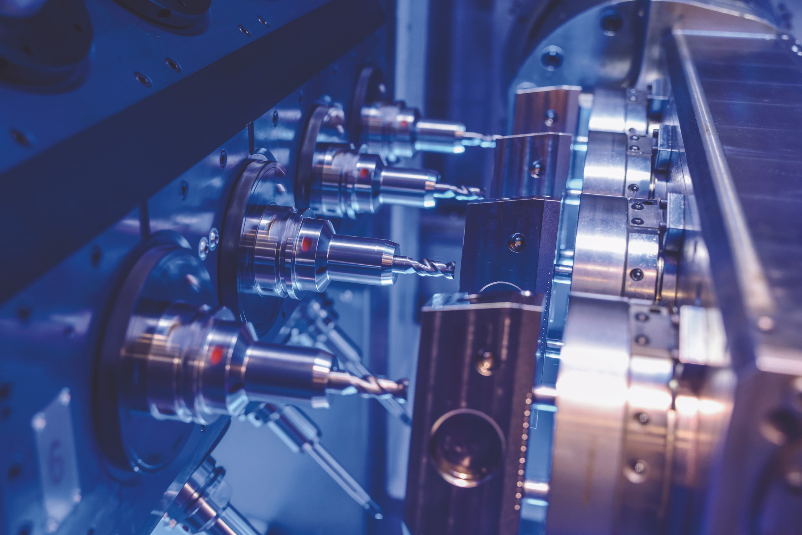 Präzision durch digitale Steuerung: Intelligente Software optimiert die Abläufe in modernen Werkzeugmaschinen und sorgt für höchste Effizienz in der Metallbearbeitung. <p>Man sieht: Nahaufnahme von mehreren metallischen Bohrern und Spindeln in einer modernen Industriemaschine, die in technischem blauem Licht beleuchtet wird.<p>