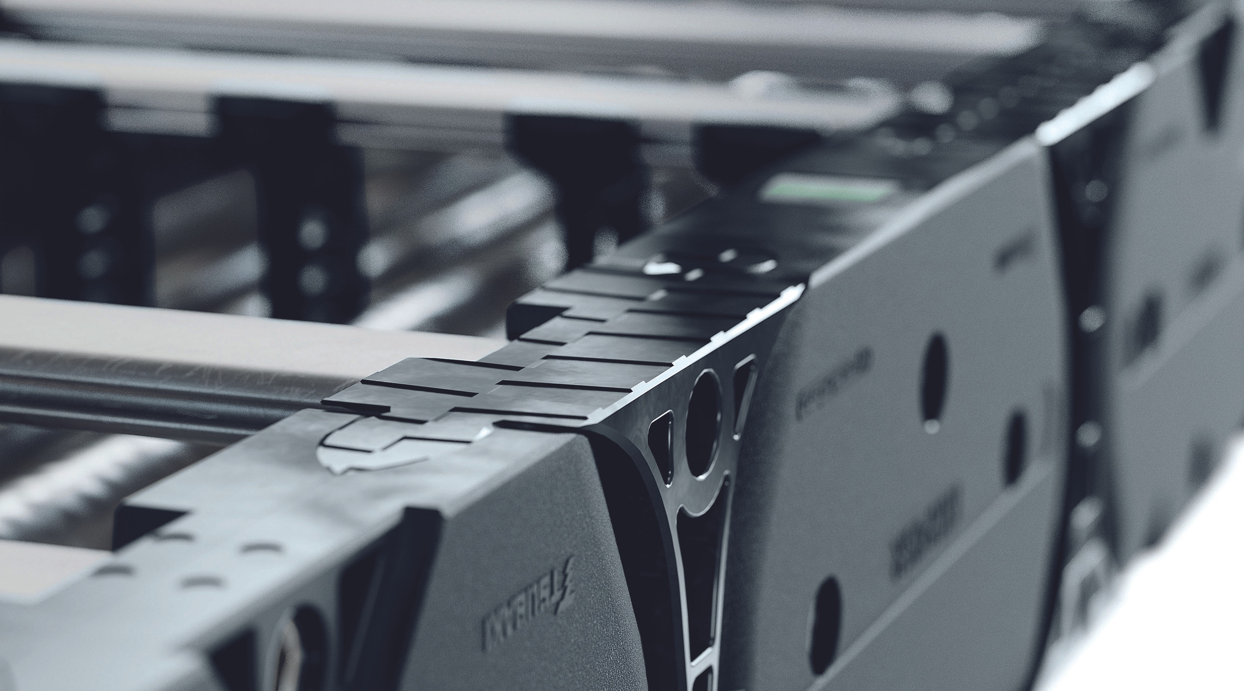 <p>Hier sieht man einen weiteren Detailbereich einer Energiekette. Die Aufnahme zeigt die Verbindung zwischen zwei Segmenten, wobei die präzise Ausführung der Teile und die strukturellen Merkmale deutlich erkennbar sind. Die Kette ist so gestaltet, dass sie sowohl Flexibilität als auch Stabilität bietet. Die Ausarbeitung der Elemente könnte auf ein durchdachtes Design hinweisen, das für die Bewegung von Kabeln und Leitungen in verschiedenen Anwendungen optimiert ist.<p>