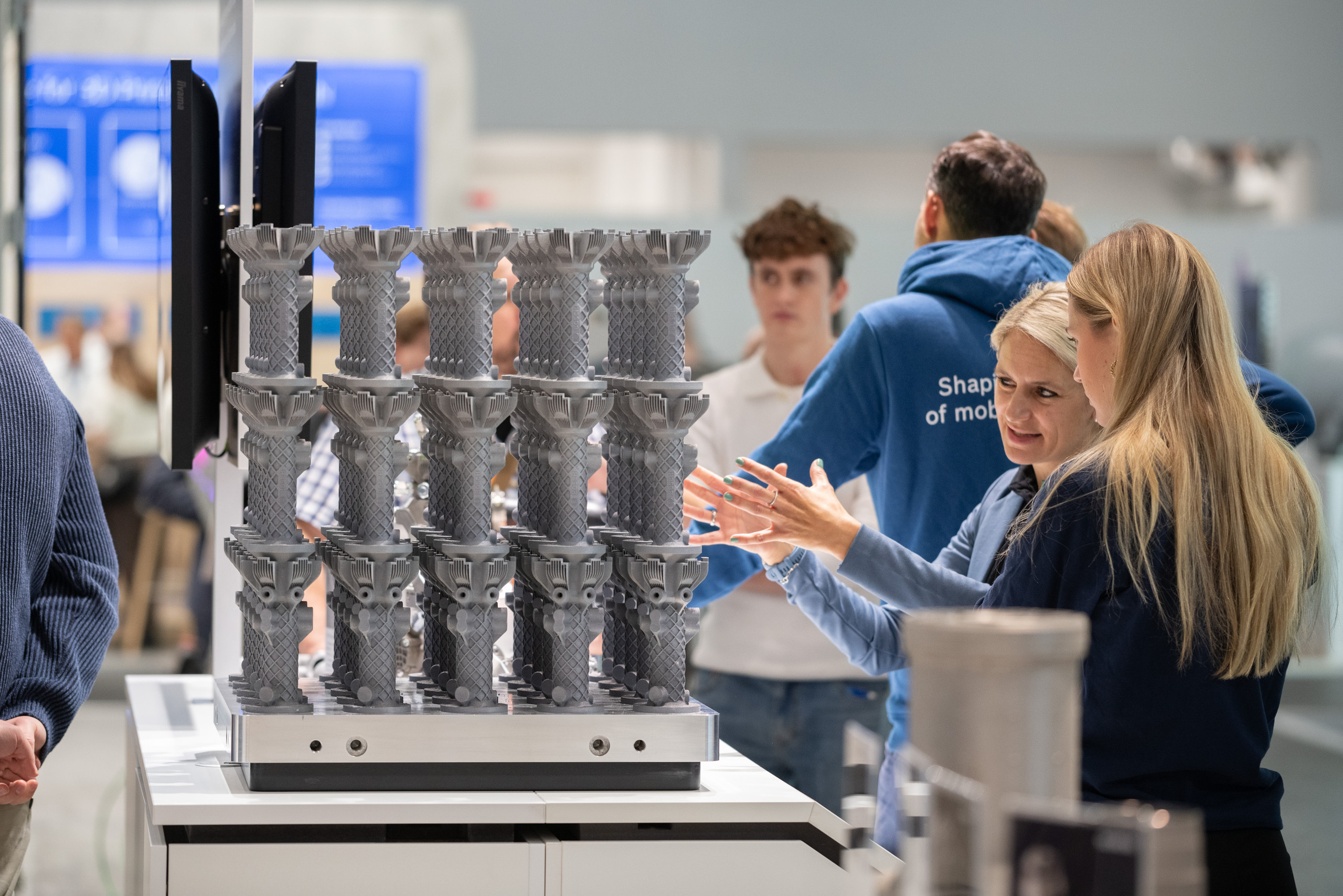 Die Aussteller betonten die hohe Besucherfrequenz, die Qualität der Fachgespräche sowie die zentrale Rolle der Formnext als Hub für Innovationen und neue Geschäftsmöglichkeiten: <p>Formnext 2025: Eine Messeszene: Im Vordergrund steht ein Präsentationsstand mit einer Bauplatte voller identischer, komplexer 3D‑gedruckter Metallteile (gitterartige Strukturen in mehreren Reihen). Daneben diskutieren zwei Besucherinnen, weitere Messegäste im Hintergrund.<p>