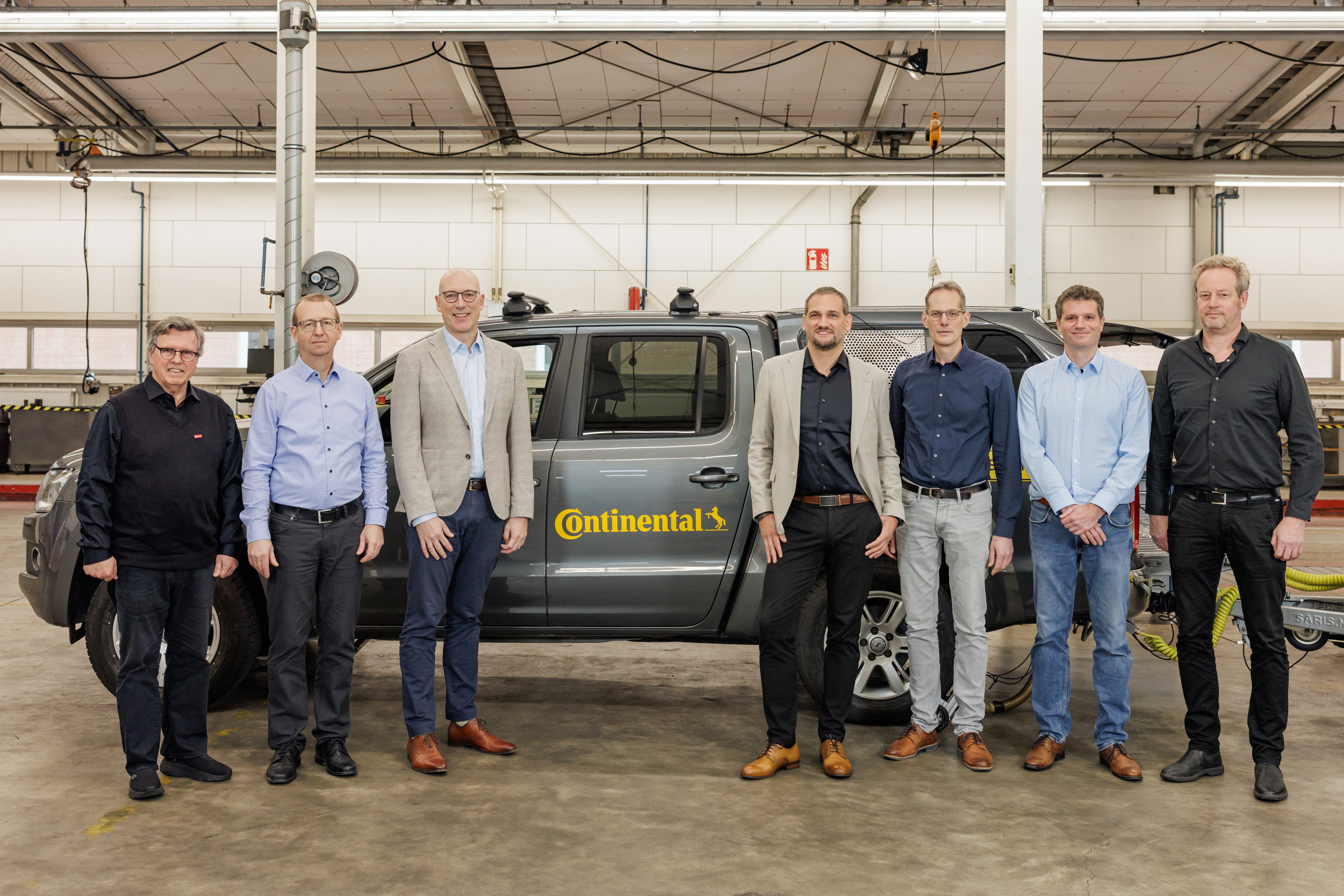 Gruppenbild mit 7 Männern, die vor einem Testfahrzeug in einer Halle stehen