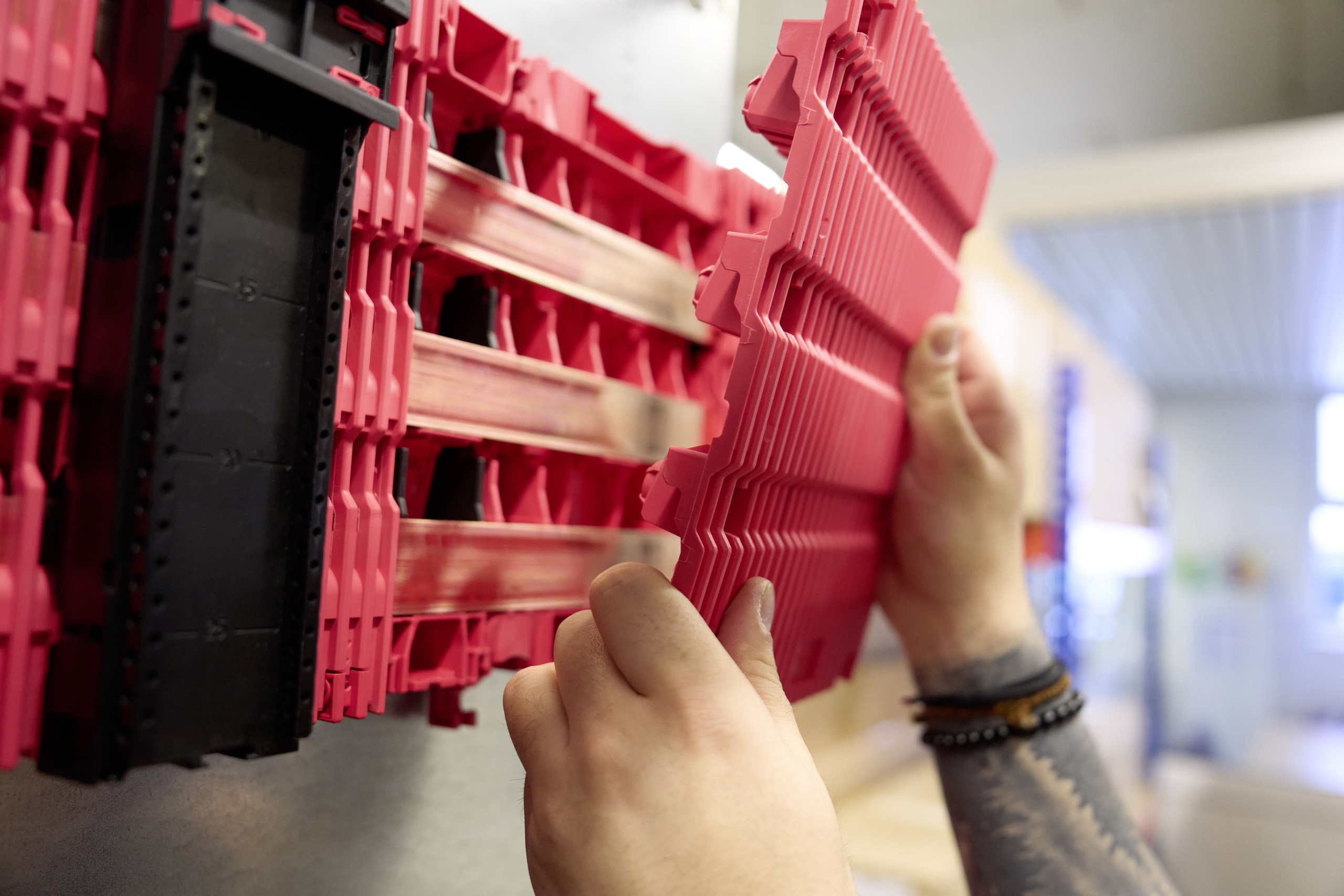 Die Schienen sitzen ohne Halterplanung sicher im Board – mit Berührungsschutz bis IP 2XB oder IP 3X. <p>Das Bild Zeigt: Zwei Hände montieren eine rote Abdeck-/Trägerplatte per Aufklicken an ein Sammelschienen-Board im Schaltschrank; dahinter sind kupferne Flachschienen und rote Rastprofile zu sehen.<p>